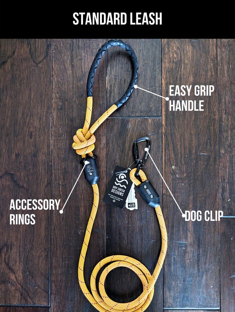 May include: A yellow and black rope dog leash with a black leather handle, a metal clip, and two accessory rings. The leash is on a wooden surface. "DRY CREEK DESIGNS" is printed on a tag attached to the leash.