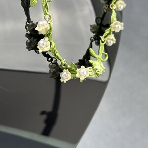 May include: A delicate green and white floral bracelet with pearl accents. The bracelet is made of metal and features a vine design with small flowers and pearls.