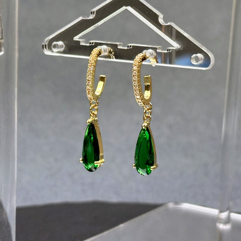 May include: A pair of gold hoop earrings with a teardrop-shaped green gemstone dangling from each hoop.