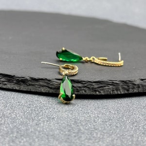 May include: A pair of gold earrings with teardrop-shaped green gemstones and a small row of clear stones around the hoop.