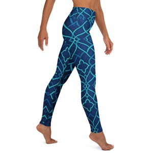 May include: Blue leggings with a geometric pattern in shades of blue and teal. The leggings feature a high waist and a repeating design of interlocking lines and floral shapes. The fabric appears to be stretchy and form-fitting.