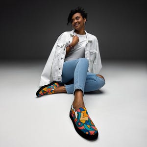 May include: Slip-on sneakers featuring a vibrant, multi-colored geometric pattern with bold black outlines, orange, teal, and pink shapes. The shoes have a thick black rubber sole and a low-profile design, showcasing a modern, abstract graphic print.