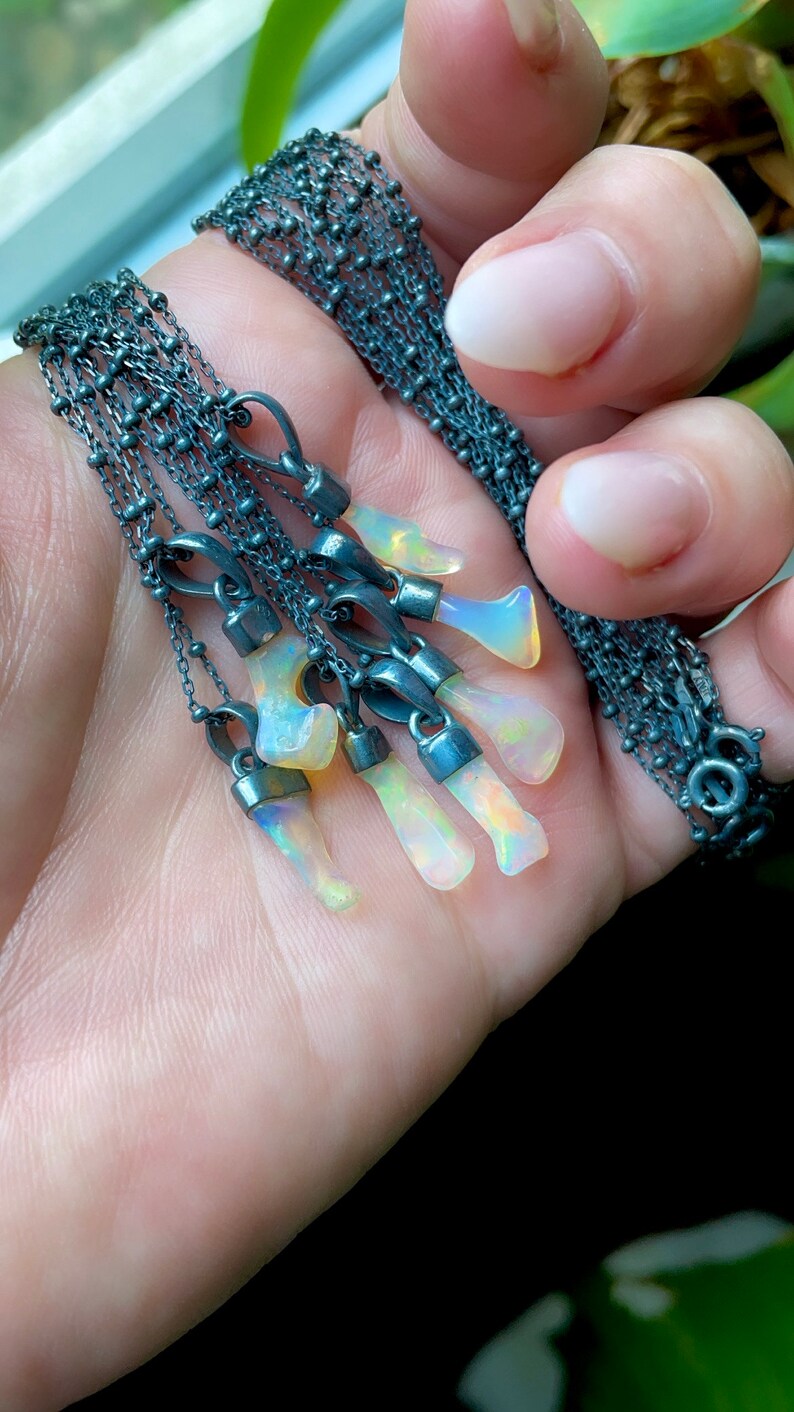 May include: A silver chain necklace with multiple opal pendants. The opals are iridescent and have a rainbow of colors.