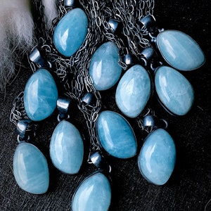 May include: A collection of aquamarine stone pendants on silver chains. The stones are a light blue color and have a smooth, polished finish. The chains are delicate and have a silver finish.