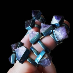May include: A set of amethyst rings with silver bands. The rings are stacked on a hand, with the amethyst stones facing outward. The stones are a deep purple color and have a slightly cloudy appearance.