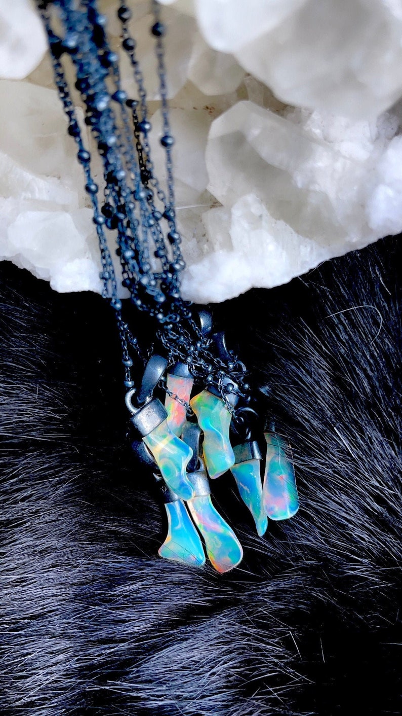 May include: A group of five iridescent opal pendants hanging from black chains. The opals are a mix of blue, green, and pink.