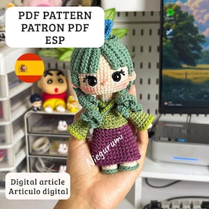 May include: A crochet doll featuring green hair, a light green top, and a purple skirt. The doll has large black eyes, a small nose, and a blue hair accessory. Text on the image reads PDF PATTERN PATRON PDF ESP, Niegurumi, and Digital article Articulo digital.