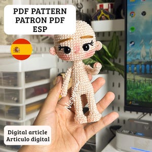 Puede incluir: Una muñeca de ganchillo beige con cabeza redonda, ojos negros grandes, cejas bordadas y mejillas rosadas. La muñeca tiene una estructura corporal simple y articulada con puntadas de hilo visibles. El texto dice PDF PATTERN PATRON PDF ESP.