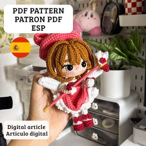 Op de afbeelding: Een gehaakte pop met bruin haar, een roze hoed en een wit met roze jurk, die een roze staf met witte en rode accenten vasthoudt. De afbeelding bevat de tekst PDF PATTERN PATRON PDF ESP en Digital article Articulo digital.