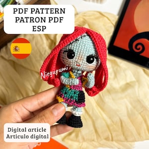 Puede incluir: Muñeca de ganchillo hecha a mano con una cara azul claro, cabello rojo y un vestido de patchwork colorido. La muñeca tiene grandes ojos negros y se sostiene en una mano. El texto en la imagen dice "PDF PATTERN PATRON PDF ESP" y "Digital article Articulo digital."