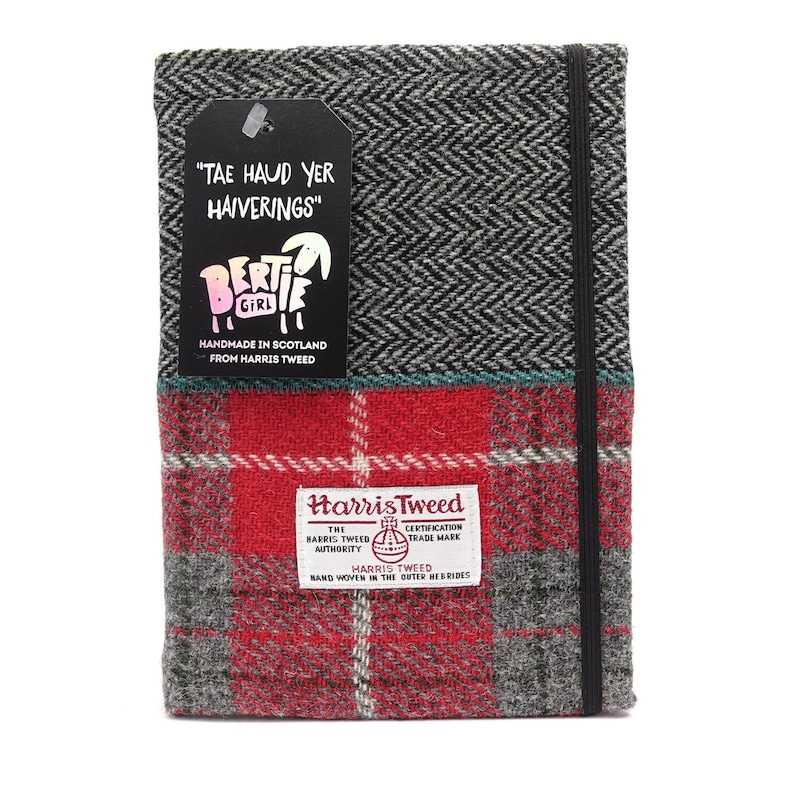 May include: A red and black plaid notebook cover with a black elastic band closure. The cover is made of Harris Tweed, a fabric woven in the Outer Hebrides of Scotland. The cover also features a black tag with the text "TAE HAUD YER HAIVERINGS" and a cartoon sheep with the text "Bertie Girl" and "Handmade in Scotland from Harris Tweed".