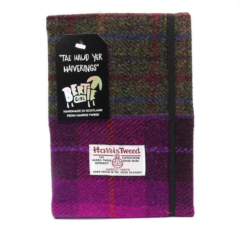 May include: A purple and green plaid notebook cover with a black elastic closure. The cover is made from Harris Tweed and has a label that reads "Harris Tweed, The Harris Tweed Authority, Certification Trade Mark, Hand Woven in the Outer Hebrides". The cover also has a tag that reads "Tae Haud Yer Haiverings" and a logo that says "Bertie Girl, Handmade in Scotland from Harris Tweed."