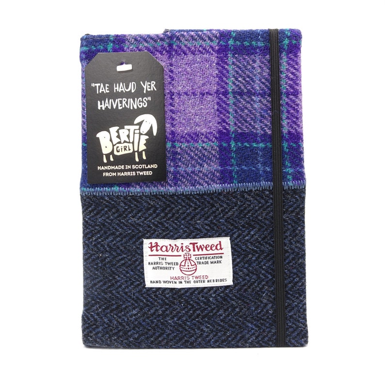 May include: A purple and blue plaid notebook cover with a black elastic closure. The cover is made of Harris Tweed and features a label with the text "TAE HAUD YER HAIVERINGS" and a sheep illustration. The label also includes the text "Handmade in Scotland from Harris Tweed".