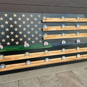 Puede incluir: Expositor de madera con temática de la bandera estadounidense, con recortes de estrellas y estantes para monedas. La bandera presenta un fondo negro con estrellas color canela, una franja verde y estantes de madera que contienen monedas.