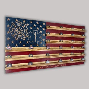 Puede incluir: Expositor de madera con diseño de bandera americana y soportes para monedas. La sección azul presenta un emblema de los bomberos y un símbolo médico. Las rayas rojas tienen estantes de madera con monedas. El texto "FIRST IN * LAST OUT" está en la parte inferior.