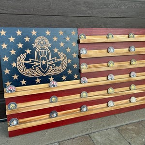 May include: Wooden American flag display with a blue star field and red stripes. Features a carved emblem and horizontal shelves holding collectible coins. The flag is made of wood and has a rustic finish.