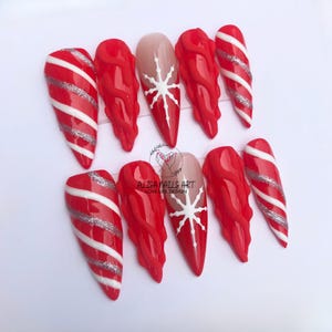 May include: Set of ten red and white candy cane themed false nails with silver glitter accents. Two nails feature a white snowflake design.  "ALISA NAILS ART LOVE LIFE DESIGN" is written in black text on a white background.