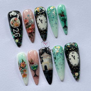 May include: A set of ten long, almond-shaped artificial nails with various designs. The designs include floral patterns, clocks, a building, and glitter. Colors include black, pink, green, and white.