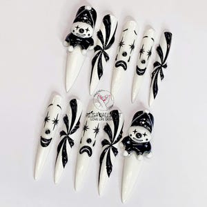 Puede incluir: Arte de uñas en blanco y negro con una cara de payaso y un diseño de lazo. Las uñas son largas y puntiagudas.