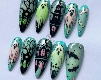 May include: A set of ten long, almond-shaped artificial nails with a Halloween theme. Each nail features a different design, including ghosts, haunted houses, bats, and trees, all in a palette of black, green, and pink.