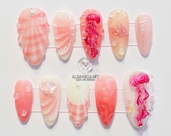 May include: Ten pink and white artificial nails with a seashell and jellyfish theme. The nails are decorated with pink and white seashells, pink jellyfish, and pearl accents.