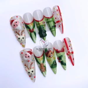 May include: Set of ten long, pointed, white acrylic false nails with a Christmas theme. The nails are decorated with green, red and white plaid, holly, candy canes, presents, a Christmas tree, Santa Claus, a reindeer, a teddy bear and a gingerbread man.