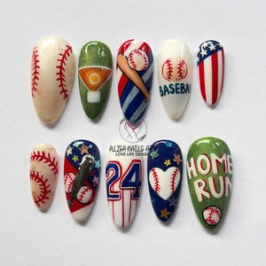 May include: A set of ten baseball-themed nail art designs. Each nail features unique artwork, including baseballs, bats, and patriotic color schemes. The designs incorporate red, white, blue, and green hues, with the words "HOME RUN" on one nail.