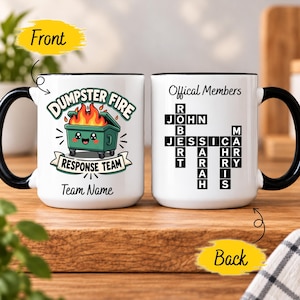 Pode incluir: Uma caneca de cerâmica branca com alça e borda pretas. A frente apresenta uma lixeira verde com fogo, o texto DUMPSTER FIRE RESPONSE TEAM e Team Name. O verso mostra uma palavra-cruzada com nomes e Offical Members.
