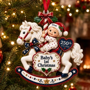 May include: A Christmas ornament featuring a white rocking horse with a blue and gold star-patterned saddle, a baby in a red Santa hat labeled Ethan, and a heart plaque reading 250th 1776-2026 and Baby's 1st Christmas with a red ribbon.
