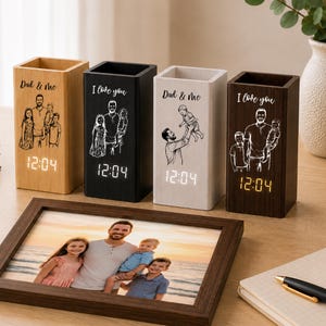 May include: Four rectangular wooden desk organisers with digital clocks displaying 12:04. Each features a laser-engraved illustration of a parent and children with the text Dad & Me or I love you. A framed photograph of a family sits in the foreground.