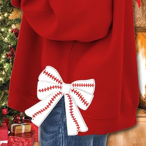 May include: Red hoodie with a white baseball-stitched bow on the back. The bow is a festive design with red stitching.