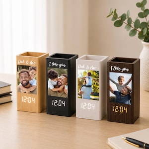 May include: Four rectangular wooden desk organizers with integrated digital clocks. Each unit features a custom photo print and white text reading Dad & Me or I Love You. The clocks display the time 12:04 in white or yellow digital numerals.
