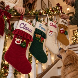 May include: Four personalized Christmas stockings hanging on a staircase railing. The red stocking features the name Clara, the dark green one says Finn, the cream one says Elodie, and the tan one says Hugo, each with festive holiday embellishments.