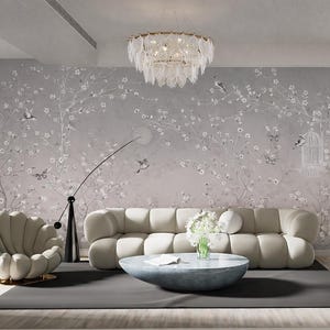 May include: A contemporary living room featuring a light grey floral wallpaper, a cream sofa, and a round coffee table. A gold chandelier hangs from the ceiling. A black floor lamp and a seashell-shaped chair complete the decor.