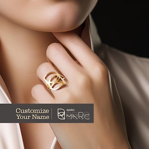 Puede incluir: Un anillo de oro con un diseño geométrico. El anillo está en el dedo de una persona. El texto "Customize Your Name" y "MARC" es visible en la imagen.
