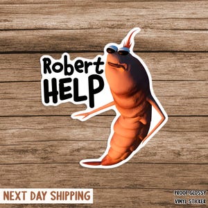 Könnte beinhalten: Glänzender Vinyl-Aufkleber mit einer cartoonartigen, garnelenartigen Figur mit Sonnenbrille. Der Aufkleber trägt die Worte "Robert HELP" in fetter, schwarzer Schrift. Die Figur ist orange und weiß, mit einem betrübten Gesichtsausdruck.