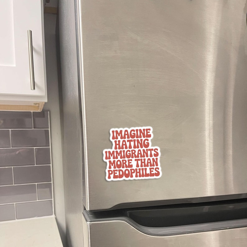 May include: A red and white sticker with the text "IMAGINE HATING IMMIGRANTS MORE THAN PEDOPHILES" is affixed to a stainless steel refrigerator door. The sticker is rectangular with rounded corners.