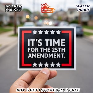 May include: A rectangular sticker with the text "IT'S TIME FOR THE 25TH AMENDMENT" in white on a black background, framed by a red border and white stars. The sticker is held by a hand against a blurred street background.