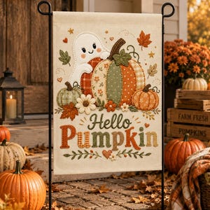 May include: A rectangular garden flag featuring a cream-colored background with a central illustration of a white ghost peeking over a large, multi-patterned pumpkin. The text Hello Pumpkin is printed below in brown and orange, surrounded by leaves.