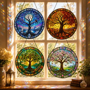 May include: Four circular stained glass suncatchers hanging in a window, each depicting a tree representing a different season: winter with a snowy landscape, autumn with orange leaves, summer with bright green foliage, and spring with pink blossoms.