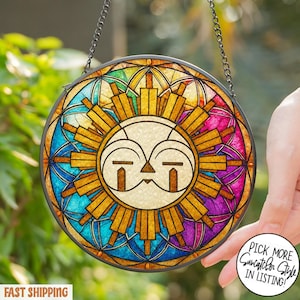 May include: Round stained glass suncatcher with a sun design. The sun has a cream-colored face with gold rays and is surrounded by a colorful border of blue, purple, and yellow. The suncatcher is hanging from a silver chain.