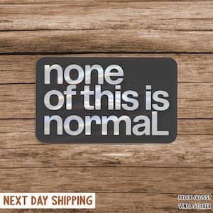 May include: A rectangular black vinyl sticker with the words "none of this is normal" in a shiny, silver font. The sticker is set against a wooden background. The words "PROOF GLOSSY VINYL STICKER" are at the bottom right.