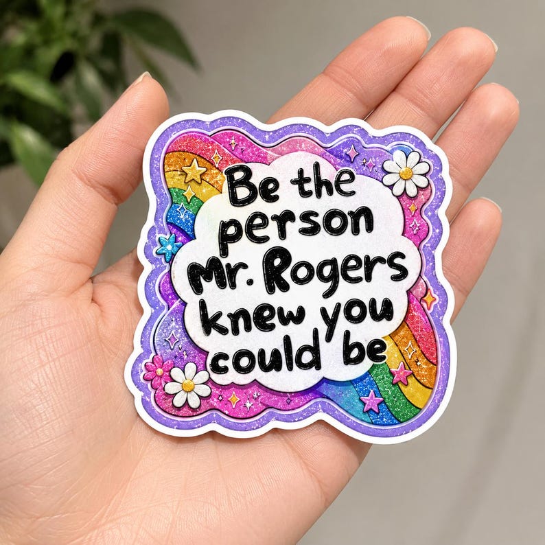 Peut inclure: Un autocollant d&eacute;coup&eacute; avec un centre en forme de nuage blanc portant le texte noir 'Be the person Mr. Rogers knew you could be'. La bordure est un motif arc-en-ciel scintillant et vibrant avec de petites fleurs roses et blanches et des &eacute;toiles sur un fond violet.