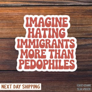 May include: A white sticker with the text "IMAGINE HATING IMMIGRANTS MORE THAN PEDOPHILES" in a retro, orange font. The sticker is on a wooden background.