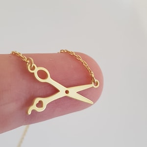 May include: A gold chain necklace with a gold scissor pendant featuring a heart cutout.