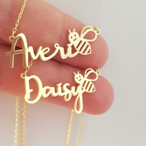 May include: Two gold necklaces with the names "Avery" and "Daisy" in cursive script. Each name is paired with a small gold bee charm.