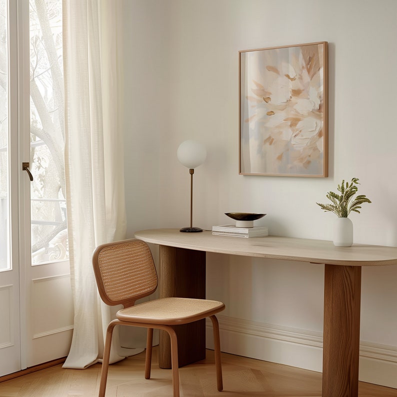 May include: A light wood desk with a white top and a white globe lamp. A woven chair sits next to the desk. A framed abstract painting with muted colors hangs on the wall above the desk.
