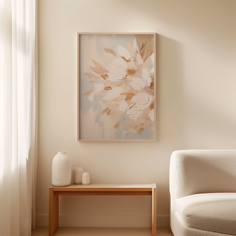 May include: A framed abstract painting with a light blue background and white and brown floral shapes. The painting is hanging on a beige wall above a wooden table with a vase and two small decorative objects.