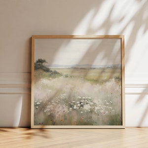 May include: A framed painting depicting a field of wildflowers with a distant view of a coastline. The painting is in a light wood frame and features a soft, muted colour palette.