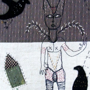 May include: A black and white embroidered artwork depicting a stylized human figure with a bird and other abstract shapes. The figure has a cross on its chest and is wearing a skirt. The background is a textured fabric.